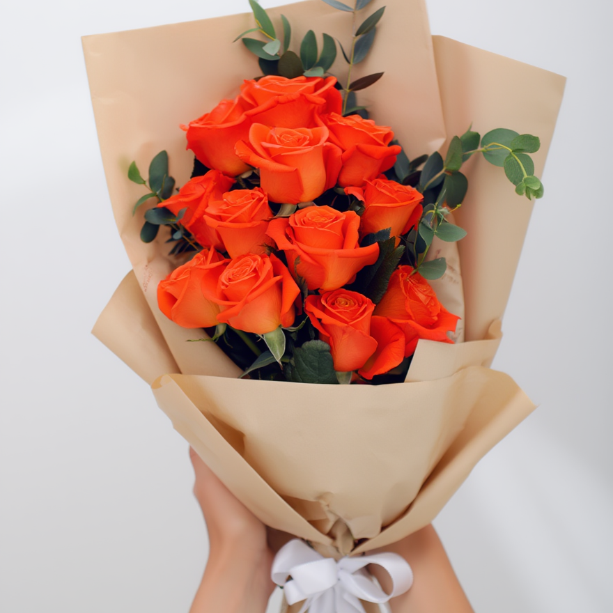 Bouquet of orange roses wrapped in brown paper with a white ribbon on a light gray background