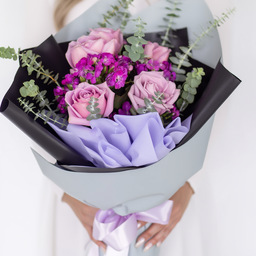 Bouquet of pink and purple flowers with greenery held by a person against a white background