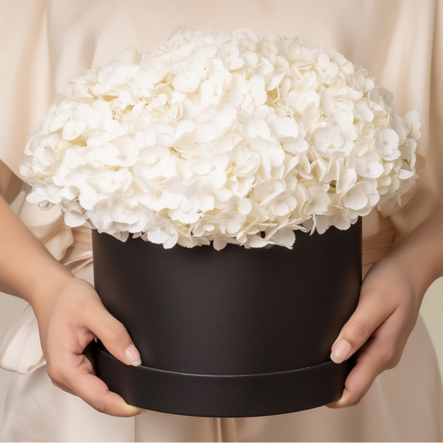 Person holding a black box with white flowers against a neutral background