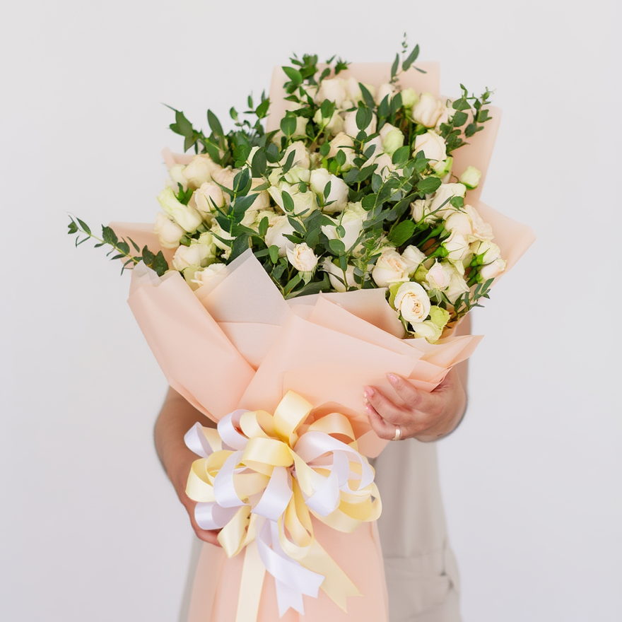 Bouquet of flowers with a decorative bow held by a person against a light background