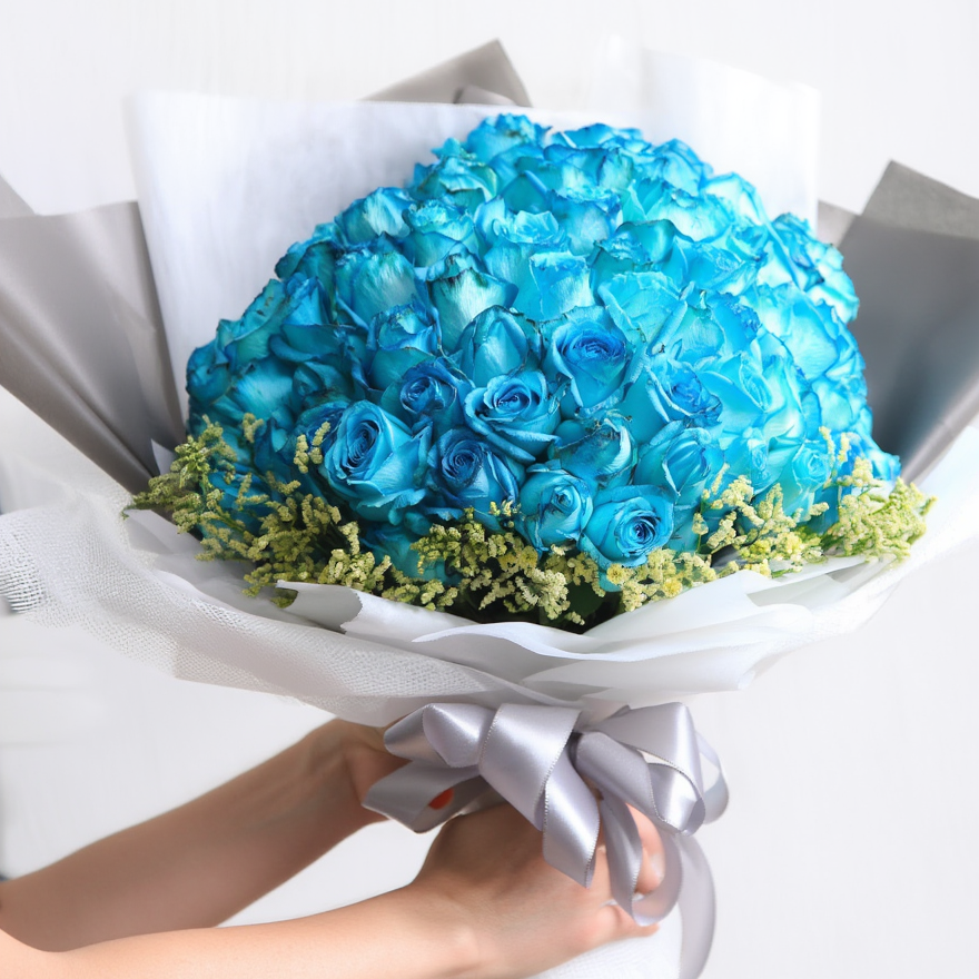 Bouquet of blue flowers wrapped in white paper with a gray ribbon, held by a person.