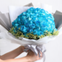 Bouquet of blue flowers wrapped in white paper with a gray ribbon, held by a person.