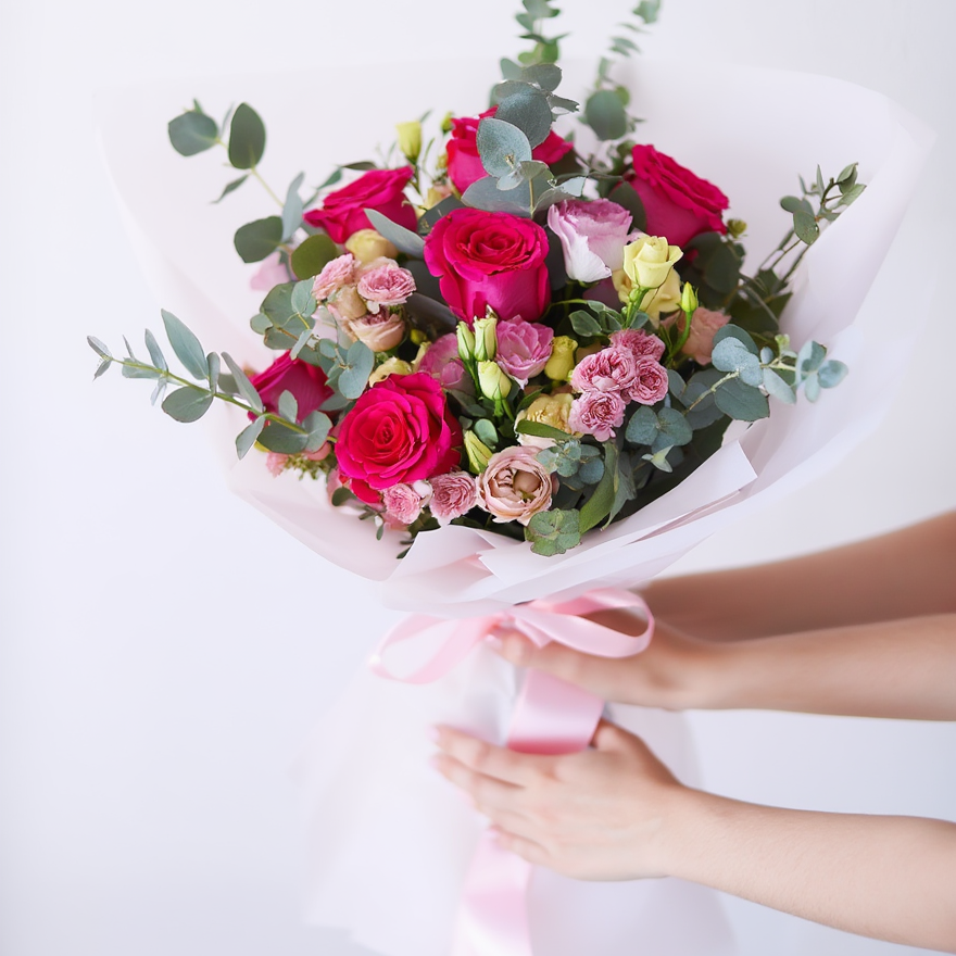 Bouquet of flowers with pink and red roses held by hands on a white background