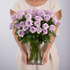 Person holding a bouquet of purple roses in a clear vase against a plain background