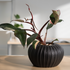 Black textured vase with a plant on a wooden surface, blurred office background