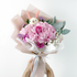 Bouquet of pink flowers with a white ribbon held by hands on a light gray background