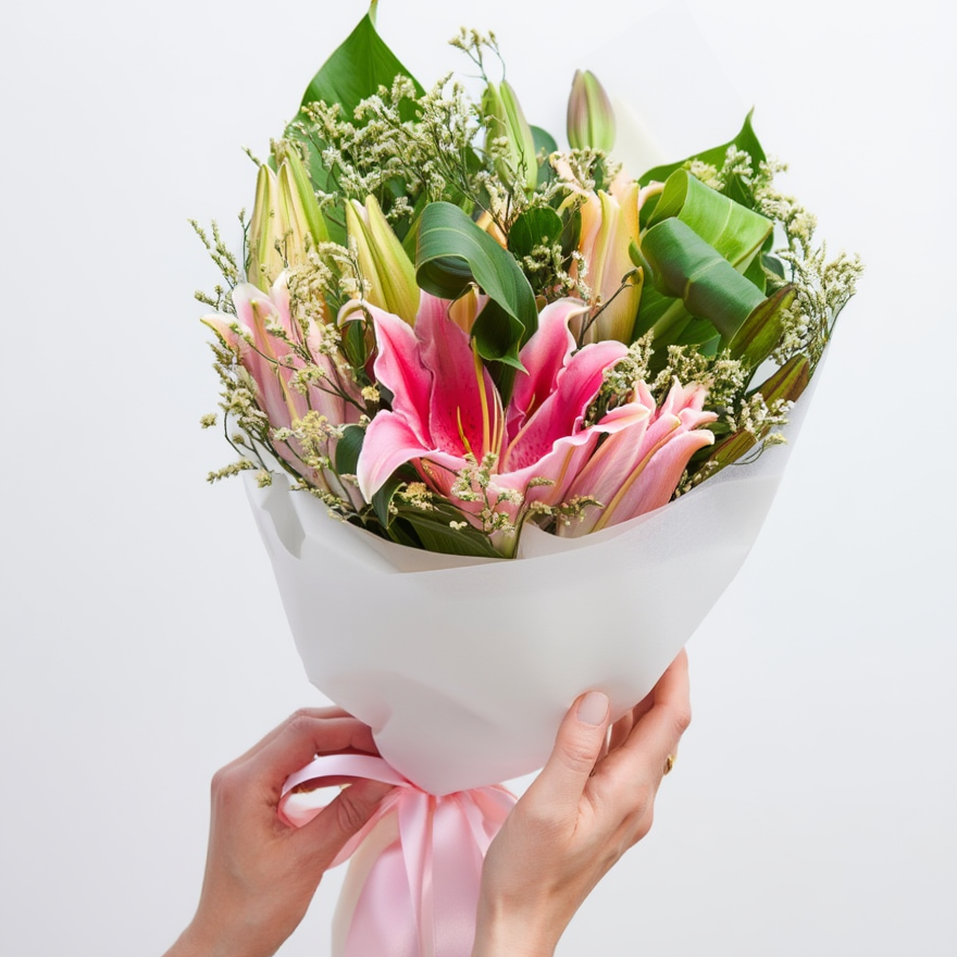 Bouquet of flowers with pink lilies held by hands against a white background