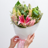 Bouquet of flowers with pink lilies held by hands against a white background