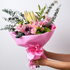 Bouquet of flowers wrapped in pink paper with a pink ribbon, held against a light background.