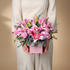 Person holding a bouquet of pink lilies in a pink box against a beige background