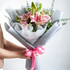 Bouquet of pink flowers with green leaves held by a person on a white background