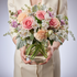 Person holding a bouquet of flowers in a clear vase against a neutral background