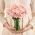 Person holding a bouquet of peach roses in a clear vase against a neutral background