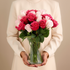 Person holding a vase of pink and white roses against a beige background