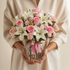 Bouquet of pink and white flowers in a clear vase held by a person wearing a beige outfit.