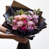 Bouquet of pink and purple flowers wrapped in black paper held by a person.