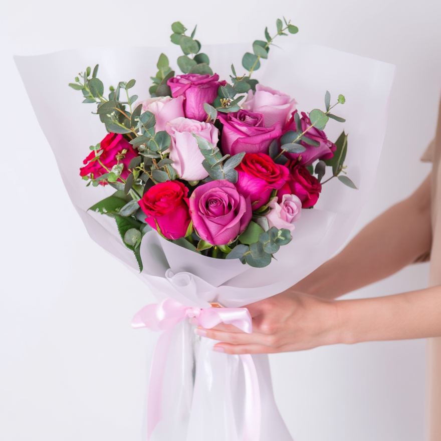 Bouquet of pink and red roses with greenery held by a person on a white background