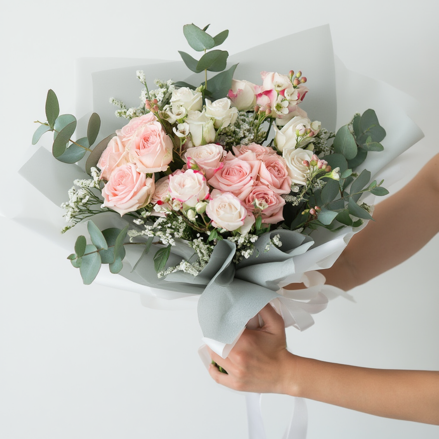 Bouquet of pink and white flowers with greenery held by a person on a light gray background