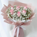 Bouquet of pink roses and baby's breath wrapped in pink paper with a white ribbon on a light background