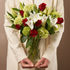 Bouquet of red roses, white lilies, and green hydrangeas held by a person in a white coat.