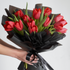 Bouquet of red tulips wrapped in black paper with a hand holding it against a light gray background