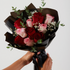 Bouquet of red and pink roses wrapped in black paper held by a person against a light gray background