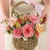 Wicker basket filled with pink and peach flowers held by a person.