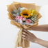 Bouquet of flowers wrapped in brown paper held by a person against a white background