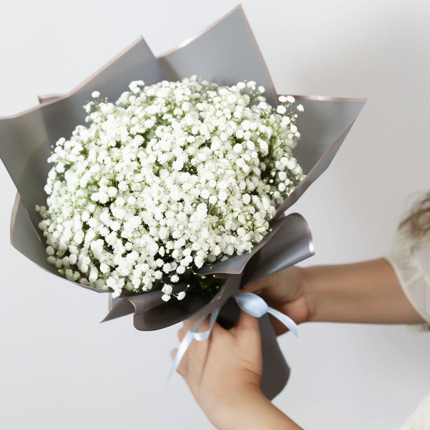 Bouquet of white flowers wrapped in black paper held by a person against a light background