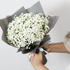 Bouquet of white flowers wrapped in black paper held by a person against a light background