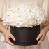 Person holding a black box with white flowers against a neutral background