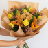 Bouquet of flowers wrapped in brown paper held by a person against a light background